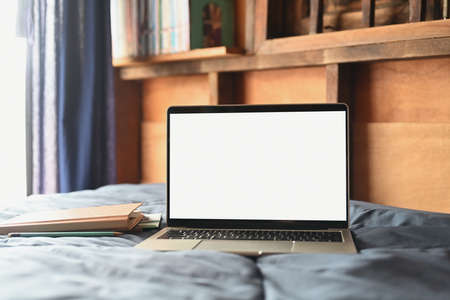 Laptop and books in cozy bedroom with soft light from window. Empty screen for advertise text.