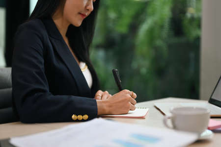 Professional millennial businesswoman sitting at her workplace and signing document.