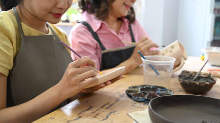 Young woman and mature woman painting painting on bowl before baking in pottery workshop.