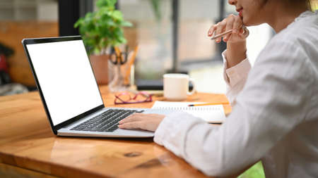 Cropped image of female employee using laptop computer on wooden office desk.