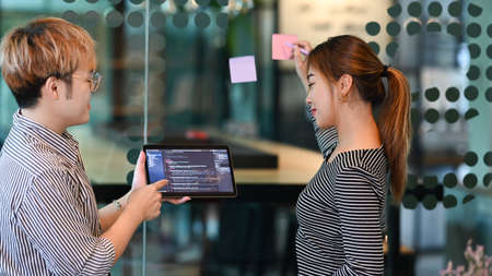 Young male software developer holding digital tablet, discussing online project with his colleagues...