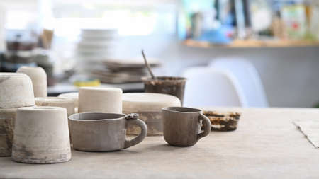 Handmade ceramic crockery, paint brushes, pottery shaping tools on wooden table in creative studio.