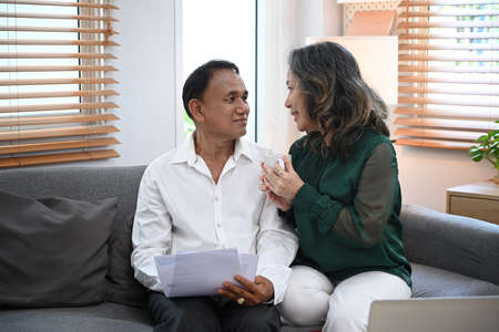 Happy senior couple using laptop, managing domestic bills together on couch at home.の写真素材