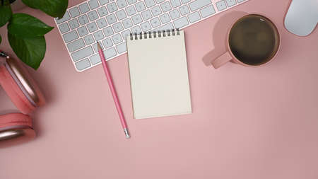Flat lay blank notebook, wireless headphone and coffee cup on pink background. Feminine workplace.の写真素材