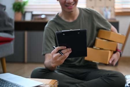 Happy small business owner preparing parcel boxes of product for shipping, working at home office. Online selling, e-commerce concept.の写真素材