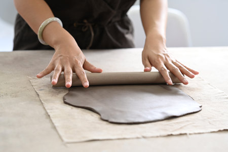 Cropped shot of ceramists using rolling pin for clay mass, making handicrafts at her studio.の写真素材