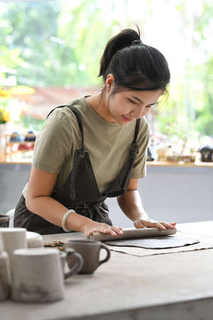 Female potter rolling pin for clay mass, making handicrafts at her studio. Creative hobby, ceramic works concept.の写真素材