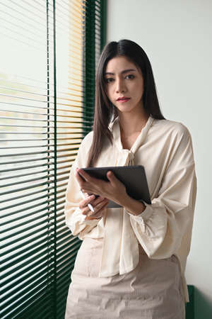 Portrait of beautiful female entrepreneur using digital tablet while standing near office window.