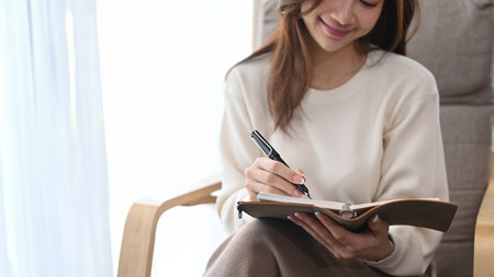 Pleasant woman in warm sweater relaxing on armchair and writing her diary.の写真素材