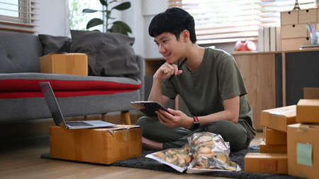 Asian male online seller using laptop for checking order on internet. Online selling, e-commerce concept.の写真素材