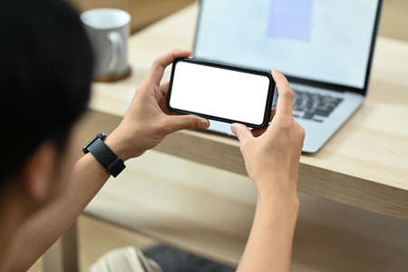Man sitting in cozy living room and using smart phone. Over shoulder view.の写真素材