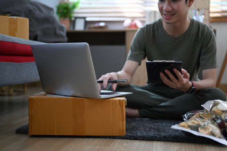 Young business man answering customers through laptops and preparing parcel boxes of product for delivery.の写真素材