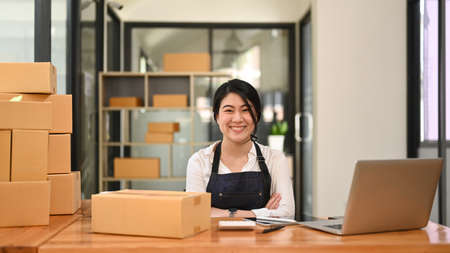 Confident young female small business entrepreneur sitting with arms crossed and smiling at camera.の写真素材