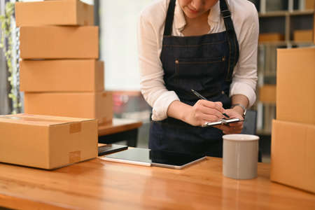 Young female entrepreneur checking product purchase order and preparing parcel for shipping....