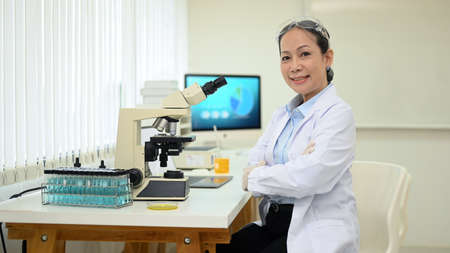 Shot of middle aged scientist sitting in front of microscope at research laboratory and smiling to...