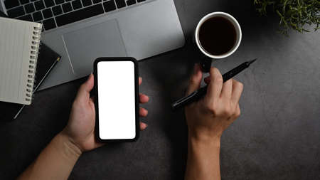 From above view man hand holding smart phone with empty display and coffee cup over black stone...