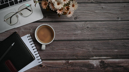 Simple workspace with laptop, eyeglasses, coffee cup and notebooks on wooden table. Copy space for text.の写真素材