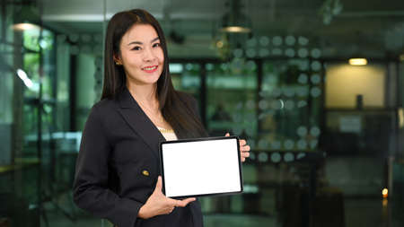 Portrait of millennial businesswoman holding digital tablet with blank display and smiling at camera.の写真素材