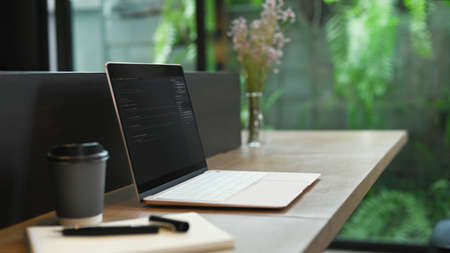 Laptop with programming code on screen, coffee cup and notebook on wooden office desk.の写真素材