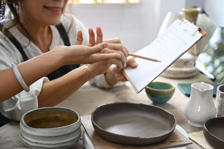 Female pottery shop owner checking purchase order, preparing product for delivery to costumer. Online selling, E-commerce concept.の写真素材