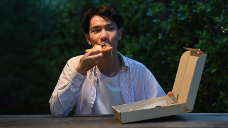 Handsome asian man enjoy eating pizza at outdoor in holiday winter night.の写真素材