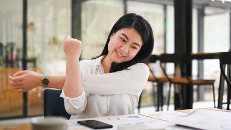 Happy asian female office worker relaxing at work and stretching her arms.の写真素材