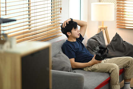 Man in casual clothes resting from playing video game with virtual reality headset, relaxing on couch at home.の写真素材