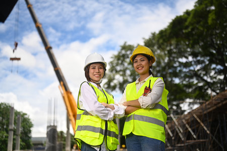 Architect and engineer wearing safety helmet and yellow vests standing at construction site with...