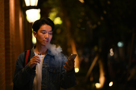 Young hipster man using mobile phone while walking through the night city streets. Night life concept.の写真素材