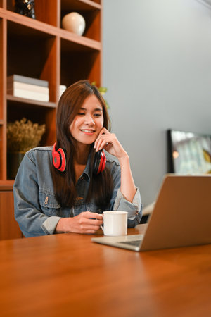 Attractive female freelancer working online or checking email on laptop, sitting in her home office.
