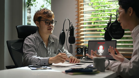 Young man radio host interviewing guest in studio while recording live podcast in studio. Radio,...