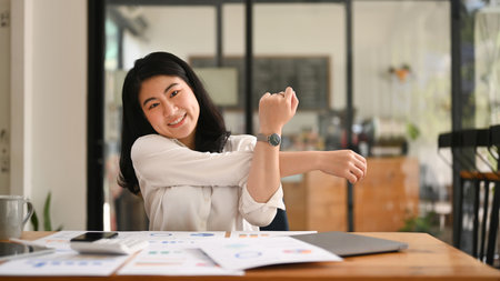 Happy female employee relaxing at work, reclining back in chair and stretching her arms.