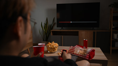 Happy man with remote control eating popcorn and watching movie in living room. Entertainment and...