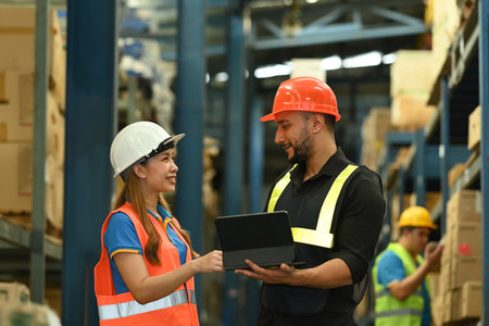 Warehouse workers in safety uniform working in warehouse full of tall shelves with goods in...