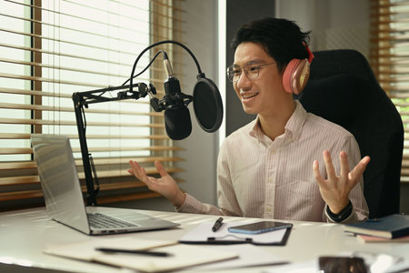 Positive asian man radio host using condenser microphone and laptop to recording podcast in small home studio.の写真素材
