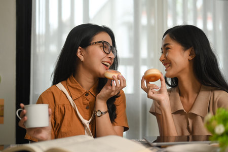 Photo of two female best friends enjoy eating delicious donuts while sitting together in coffee shop.の写真素材