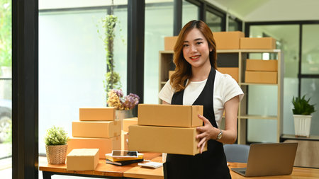 Attractive woman entrepreneur wearing apron holding cardboard and smiling to camera. Online selling, E-commerce concept.の写真素材