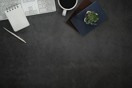 Flat lay modern workspace with wireless keyboard, notepad, coffee cup and succulent plant on black...
