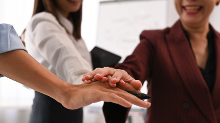 Close up image of successful businesspeople stacking hands together. Teamwork, collaboration and...
