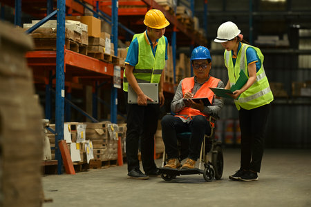 Male manager in wheelchair and workers working together in warehouse. Manufacture storehouse occupation concept.の写真素材