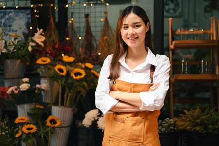 Startup small business entrepreneur in apron standing with arms crossed at her florist shop and smiling confidently to camera.の写真素材