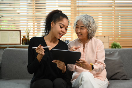 Smiling retried woman and her granddaughter surfing internet on digital tablet together on couch. Retirement, technology concept.の写真素材