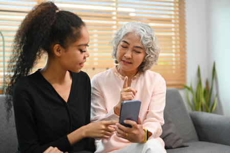 Grownup daughter teaching interested retired mother using social networks on smart phone. Elderly, technology concept.の写真素材