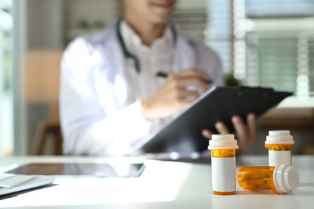 Medical pill bottles with blank label on white table and female doctor sitting in background.の写真素材
