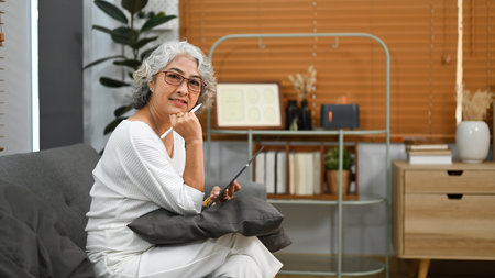 Pleasant elderly woman browsing wireless internet on digital tablet, relaxing on couch at home.