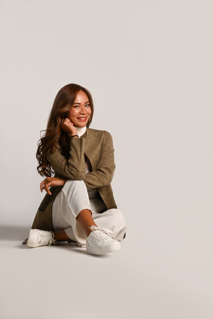 Portrait of beautiful young woman in stylish jacket sitting on white background. Autumn fashion concept.の写真素材