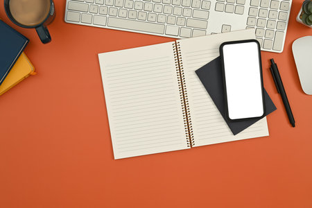 Top view smart phone with blank screen, notepad, coffee cup and keyboard on orange background.の写真素材
