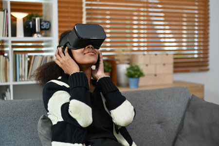 Teenage woman playing video games on virtual reality headset while sitting on couch. Futuristic technology concept.の写真素材