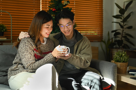 Happy young couple relaxing and drinking hot chocolate on couch, spending winter holidays together in cozy home.の写真素材