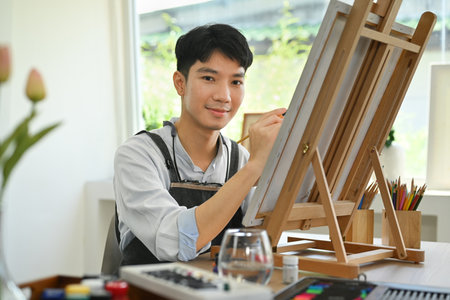 Handsome male artist painting with watercolor on canvas at home studio workshop. Art and leisure activity concept.の写真素材